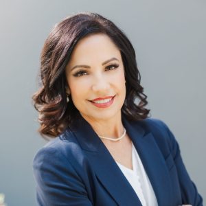 A woman - Kathryn Hamel in a blue jacket standing with arms crossed.